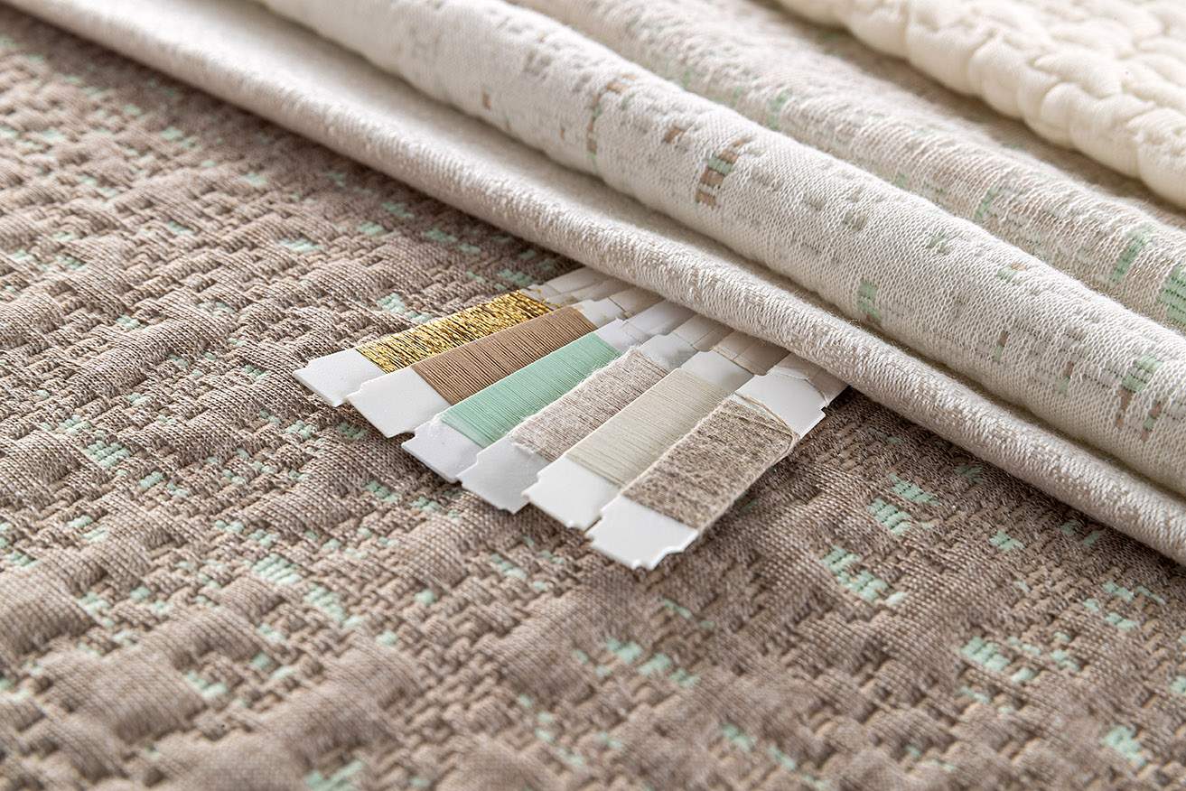 一块整洁地展示着的象牙色与浅棕色织物，上面绑着用彩色丝线缠绕的木棍，展示了多种颜色选择。 