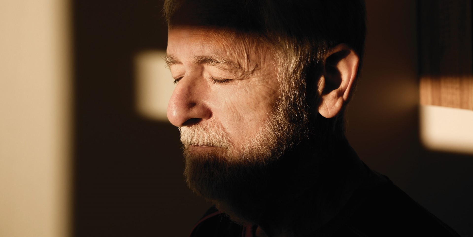 Un hombre mayor con los ojos cerrados bajo la cálida luz del sol, respirando libremente el aire limpio y fresco, disfrutando de un momento de tranquilidad