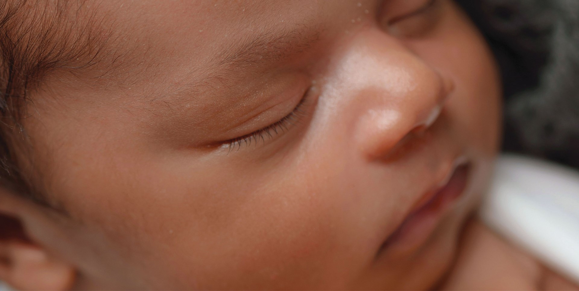 Retrato en primer plano de un bebé dormido con rasgos faciales serenos en una iluminación suave, transmitiendo una sensación de sueño confortable