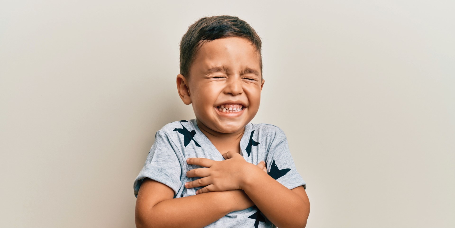 Niño riendo a carcajadas y agarrándose el pecho con los ojos cerrados tras una buena noche de sueño.