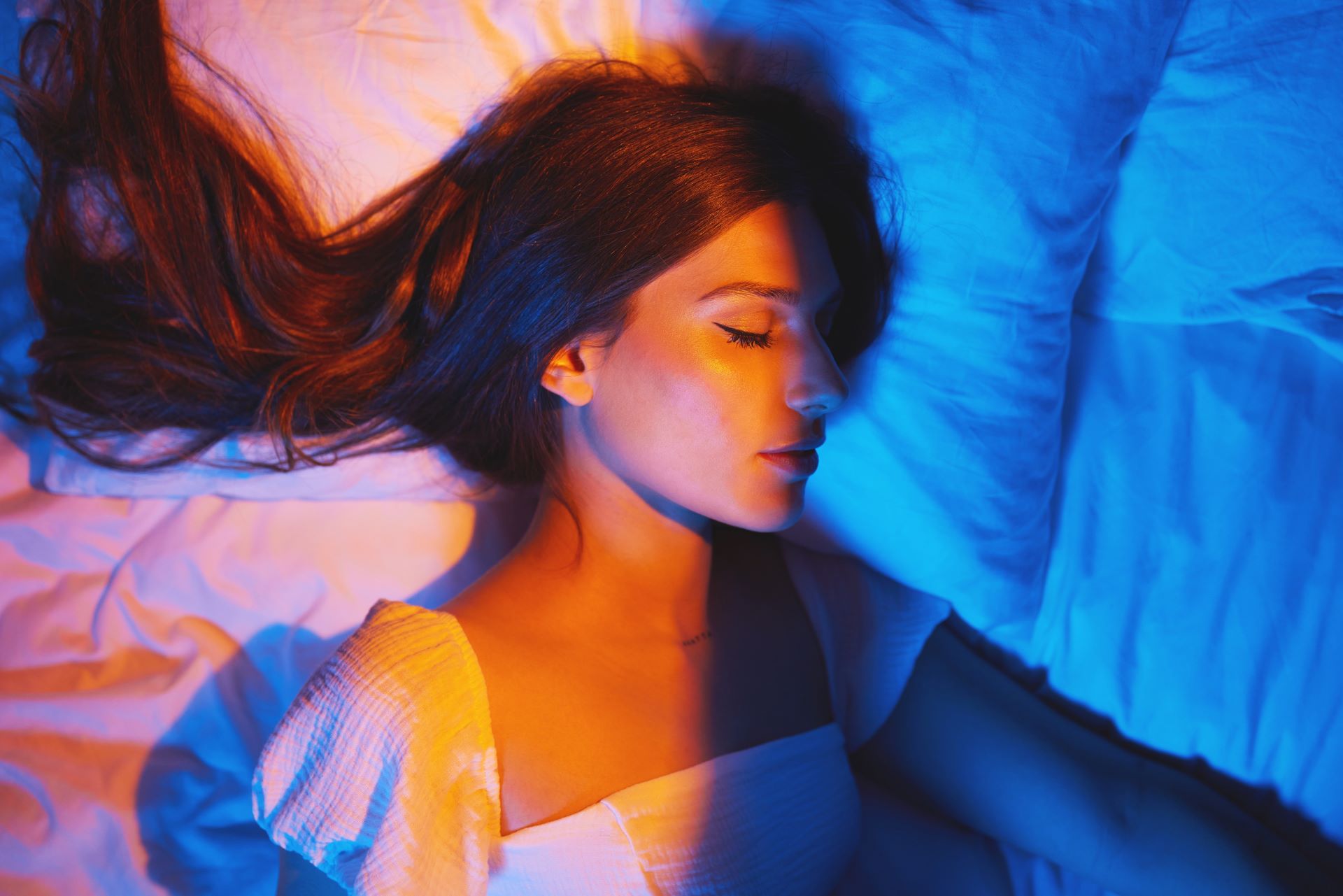 A lady sleeping on her side, with her face split by soft gold and light blue shades. 