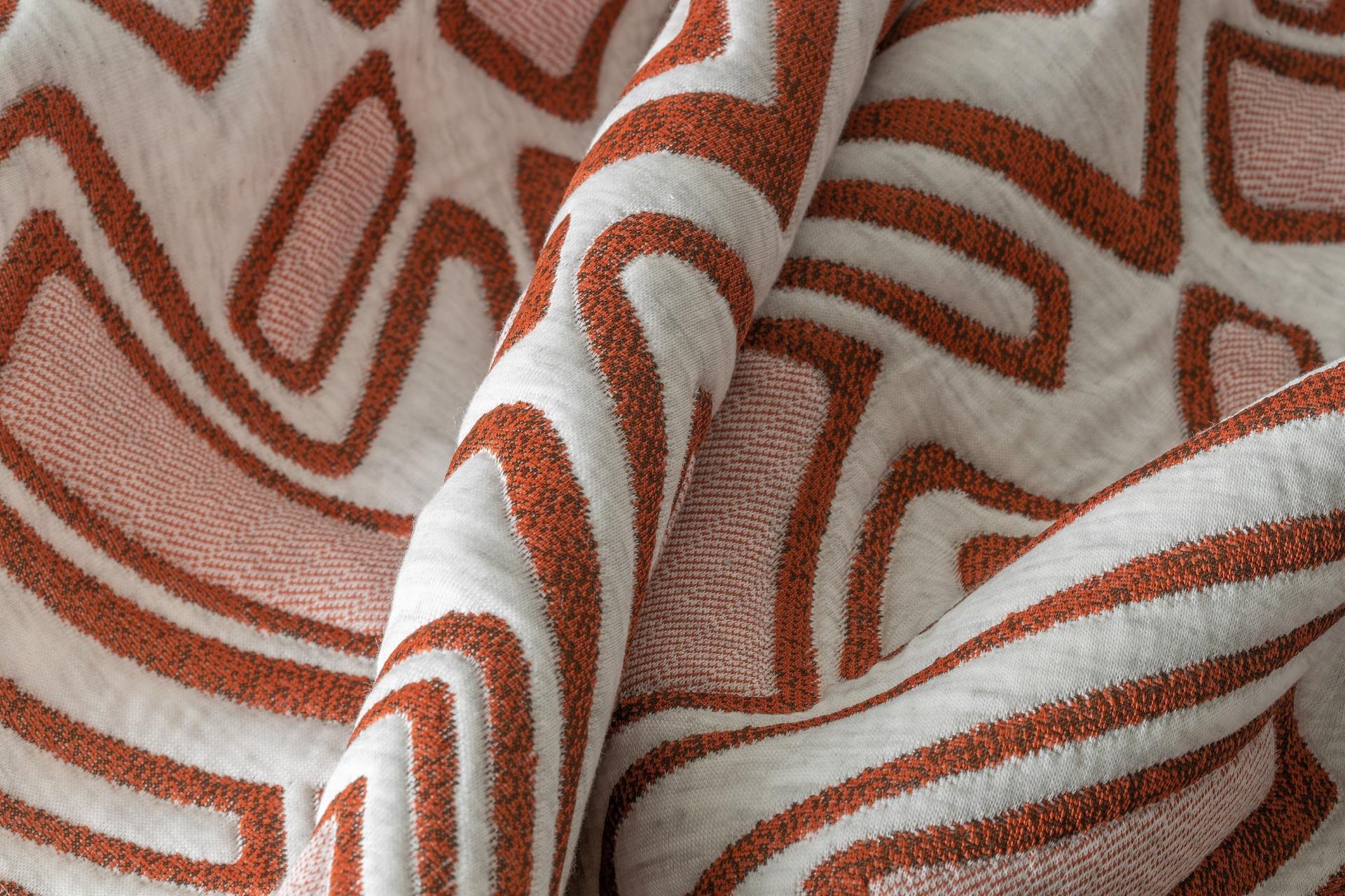 Close-up of fabric featuring bold, textured red patterns on a soft white background.