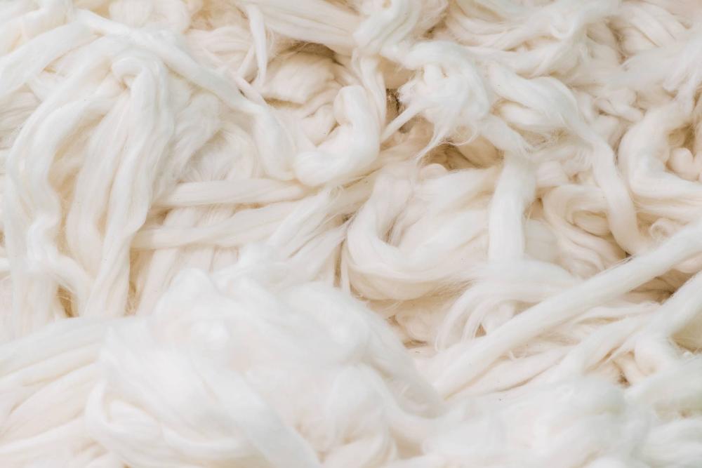 Close-up of beige recycled cotton yarn, showing its natural, fluffy texture.