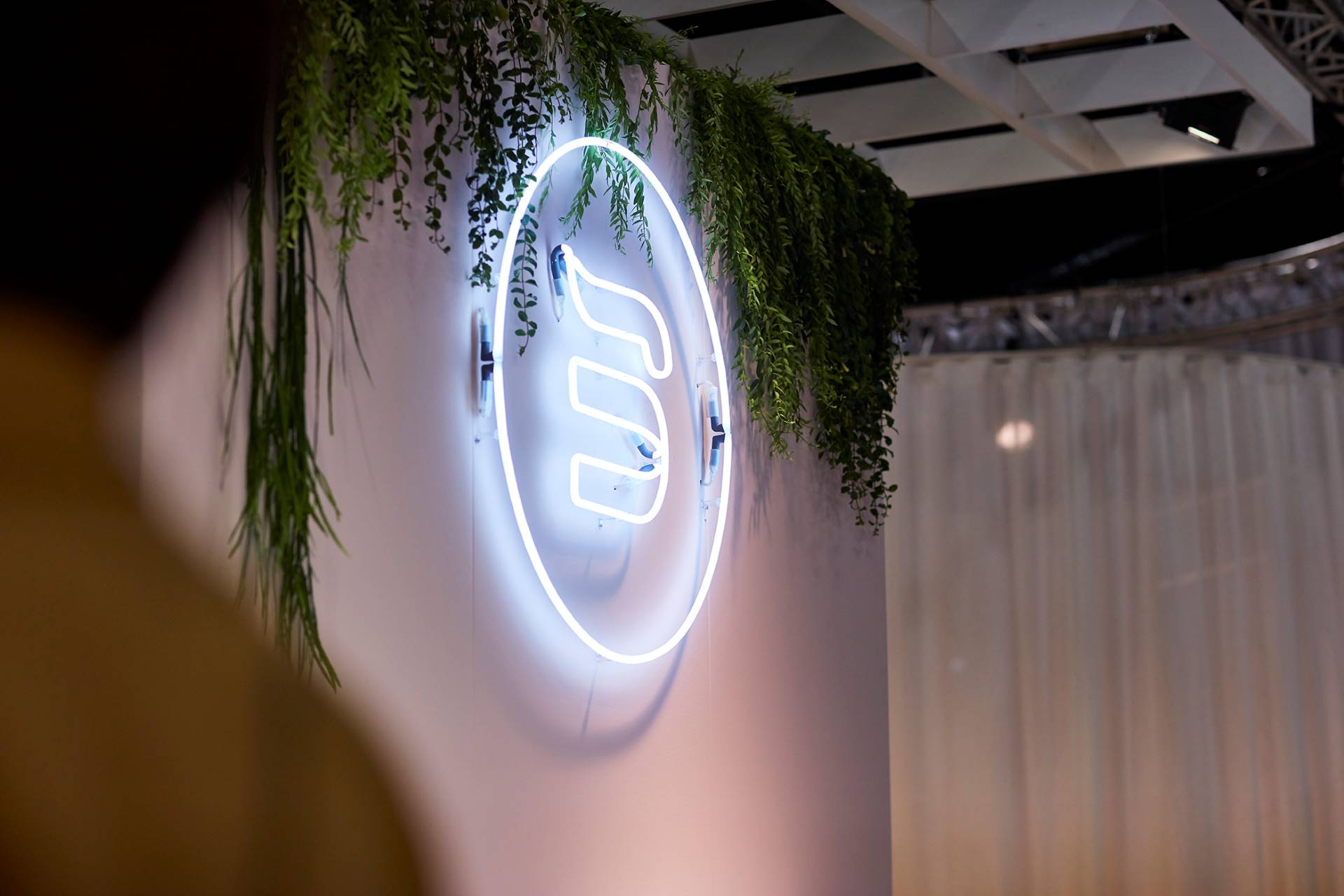 Large neon BekaertDeslee logo on a wall surrounded by greenery