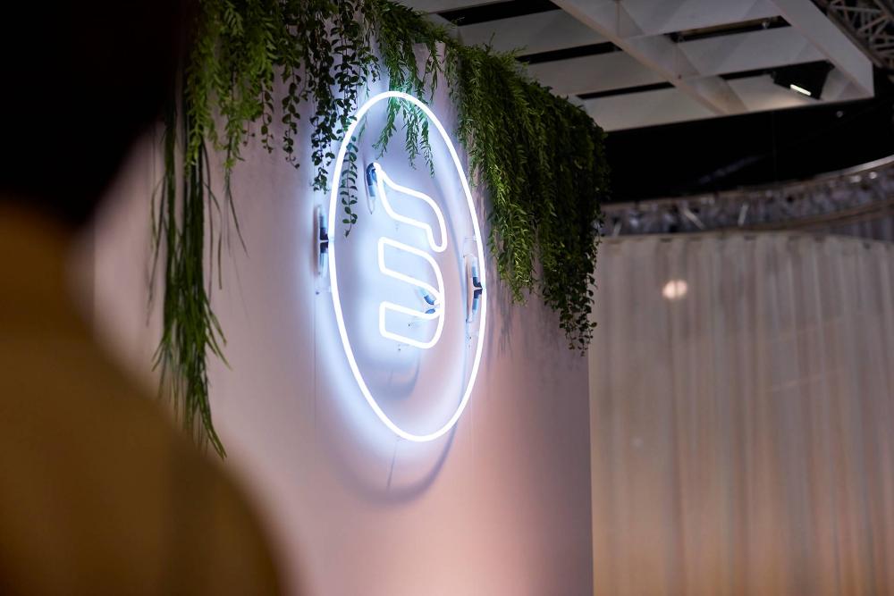 Large neon BekaertDeslee logo on a wall surrounded by greenery