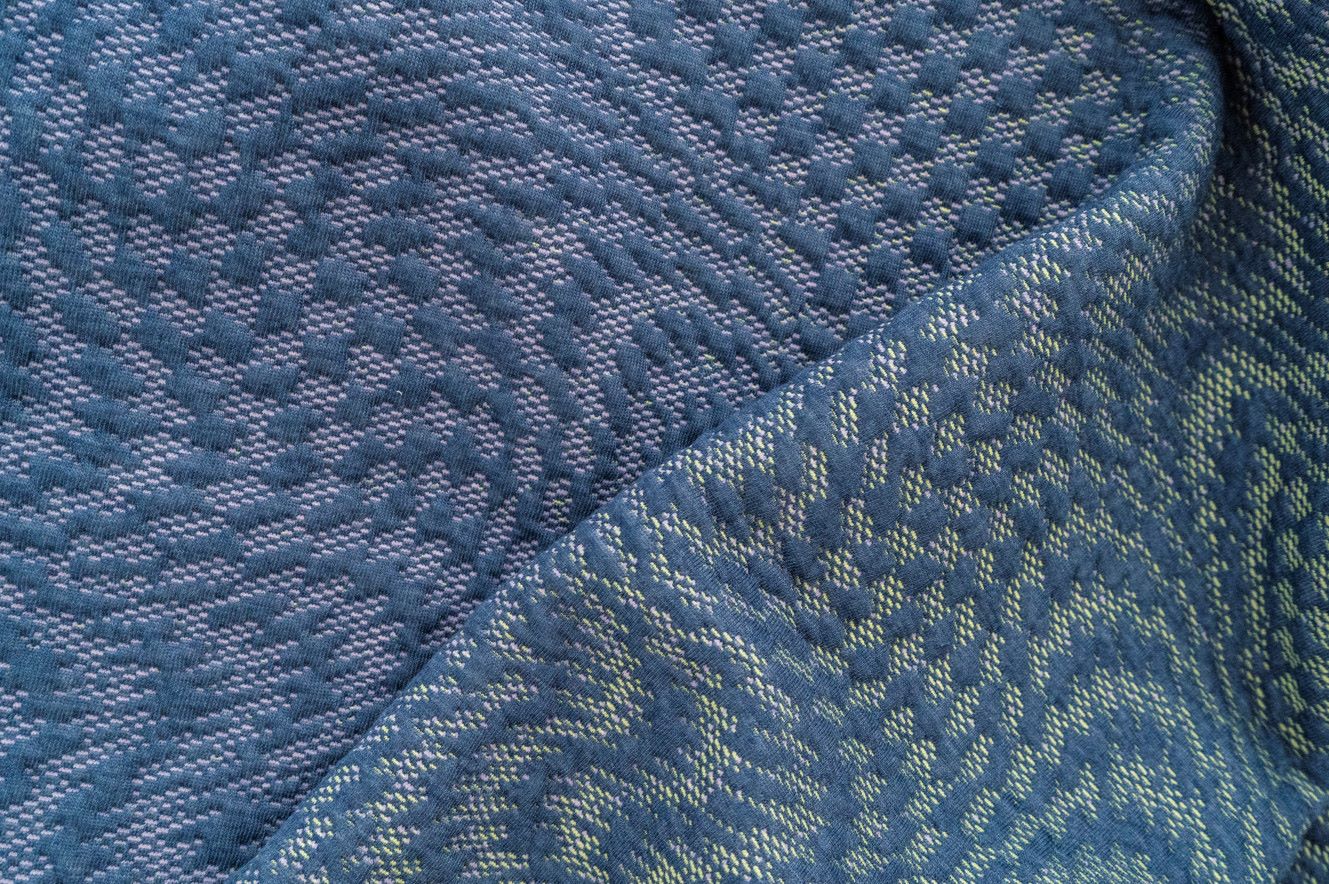 Close-up of a textured fabric with a subtle geometric pattern in shades of blue, purple, and yellow.