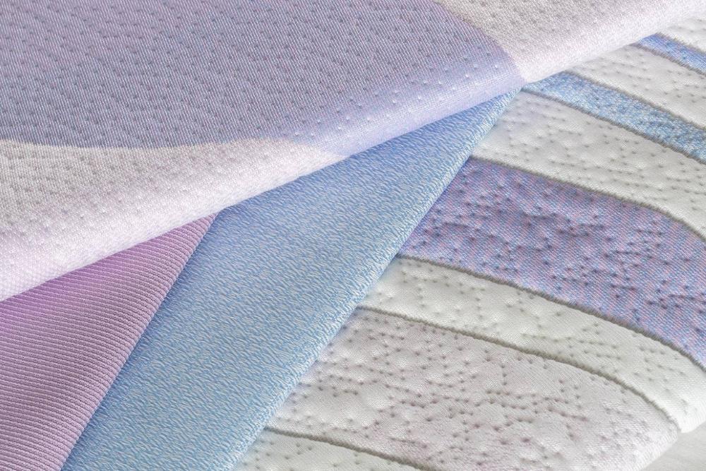 Soft-toned mattress fabric samples in light purple and blue with wavy textured patterns