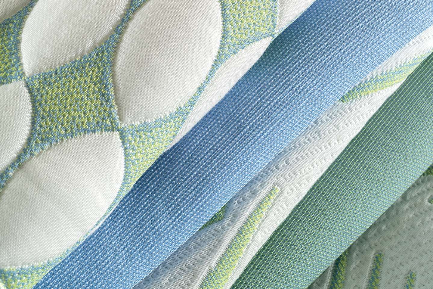 Layered textiles in soft blue, green, and white with rich textures and intricate weaves.
