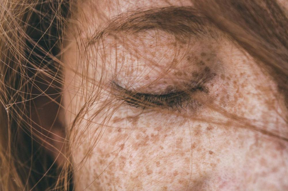 Close-up of a girl's face with closed eyes, freckles and flowing hair strands.