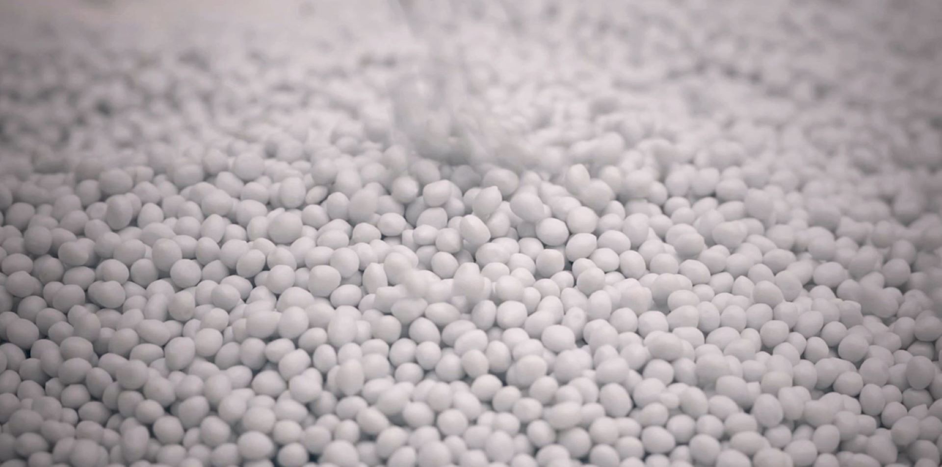 Recycled yarn material in a form of numerous small white granules, used for sustainable mattress textiles.