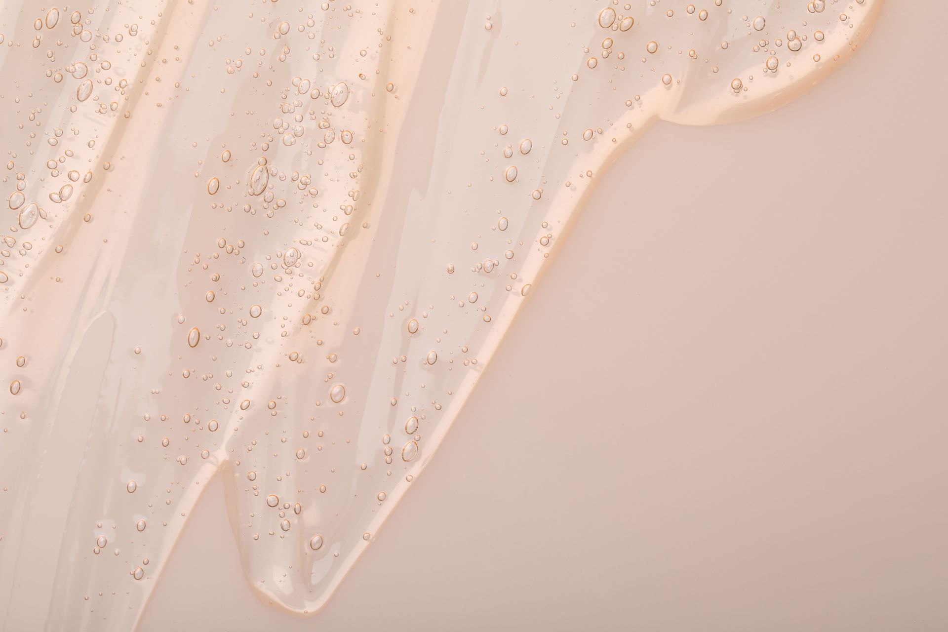 Close-up of a clear liquid with bubbles on a beige background representing skincare protecting and restoring properties.
