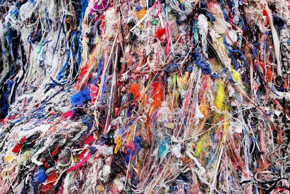 Piled polyester textile waste in various colors used for recycling.