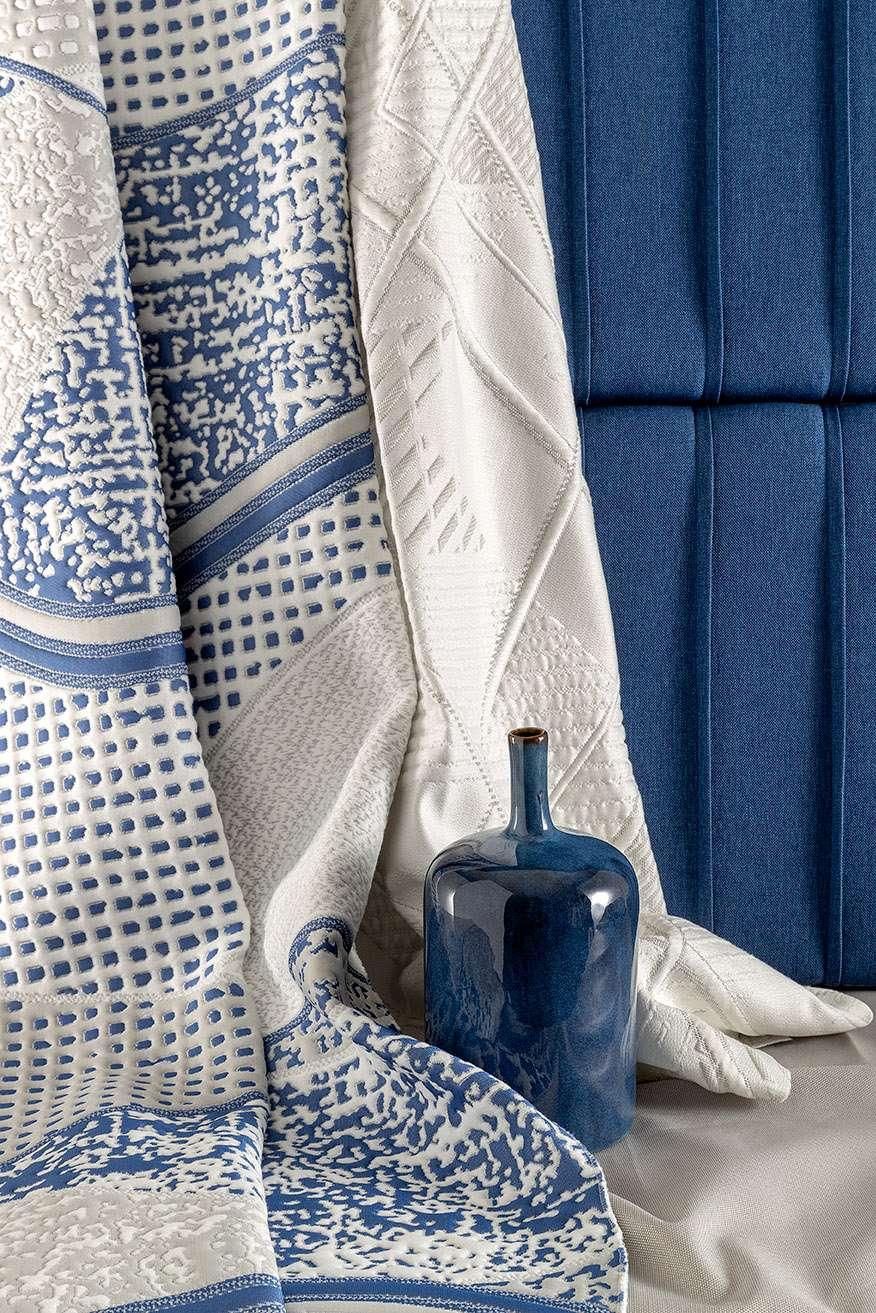 Artistic arrangement of intricately patterned, blue and white mattress fabrics with a ceramic vase